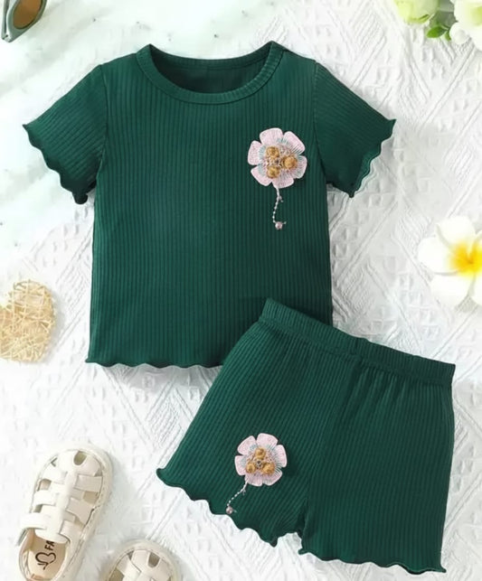 Green children's outfit with floral design on a textured white surface