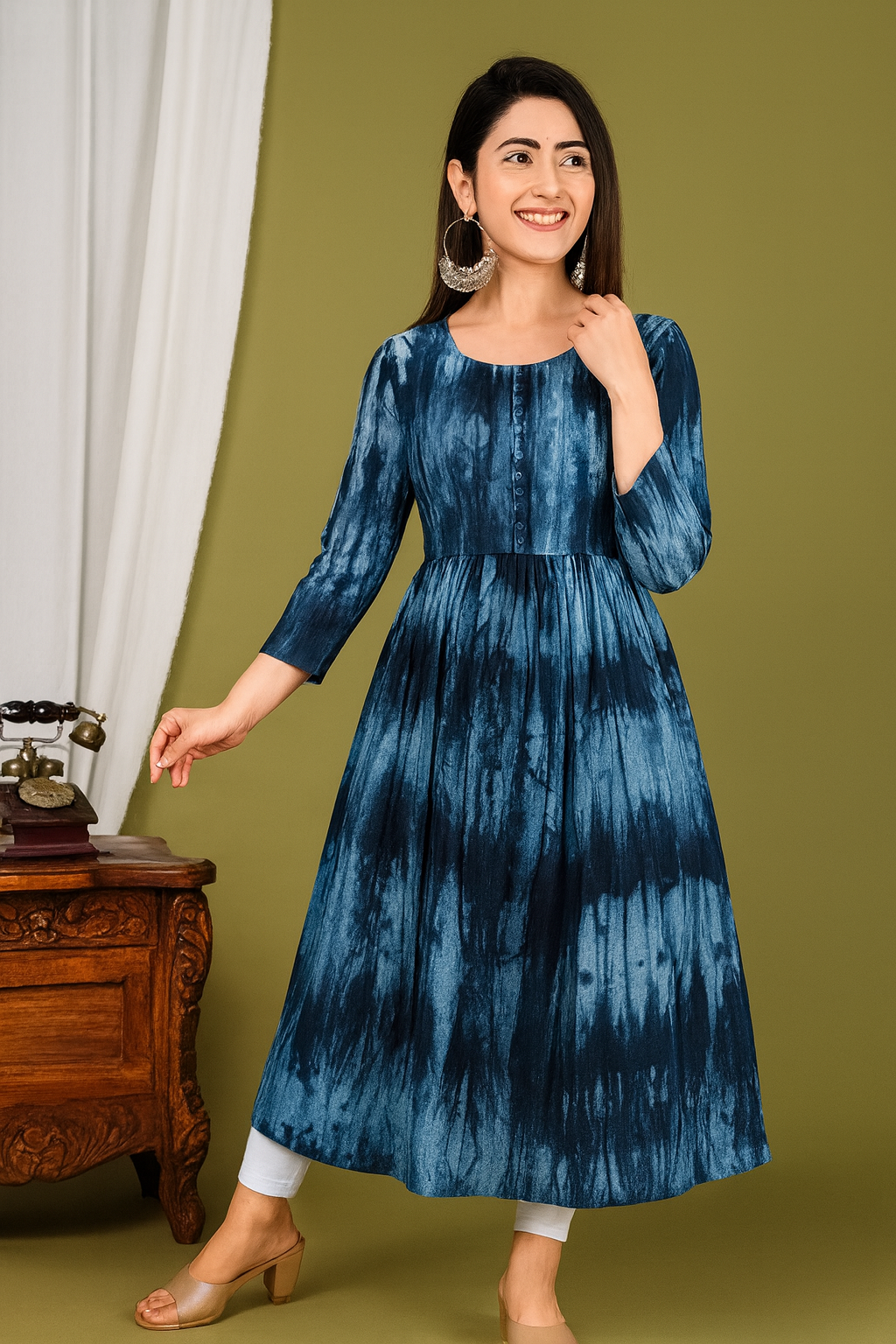 Woman wearing a blue tie-dye dress standing against a green wall.